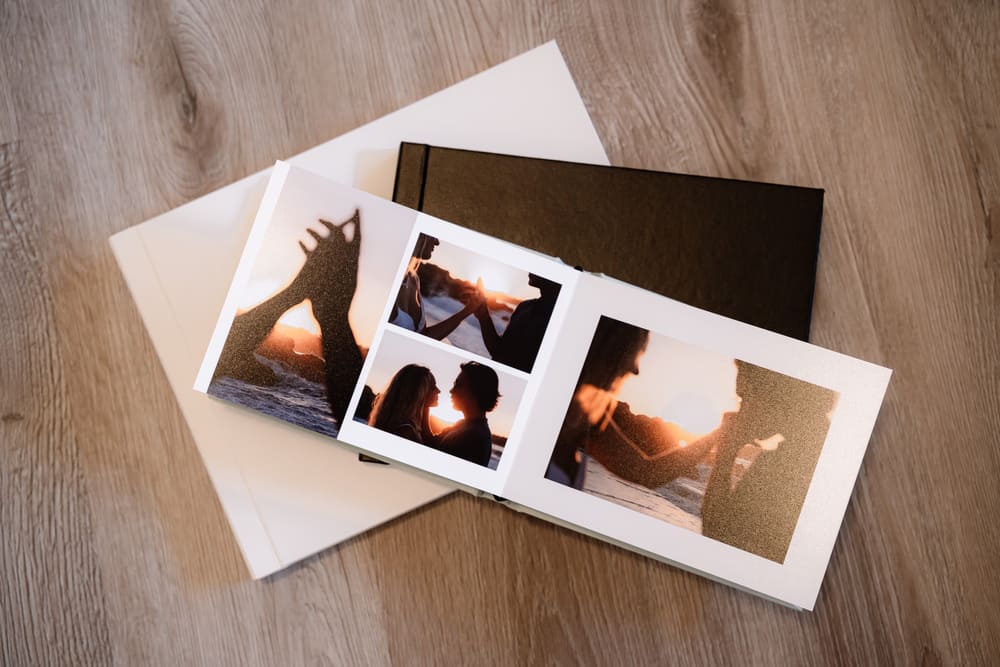 album di matrimonio che contiene le foto del servizio fotografico di matrimonio degli sposi. giace aperto sul pavimento di legno e mostra degli scatti al tramonto della coppia