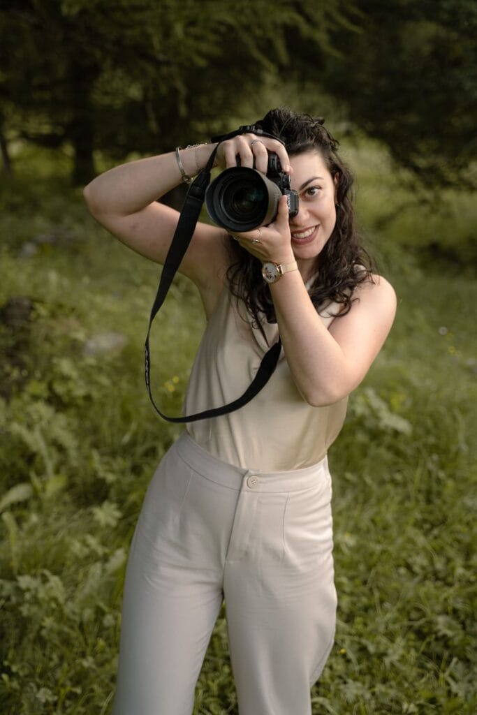 Fotografa di matrimonio a Torino di nome Eleonora Todaro. Regge una macchina fotografica in mano mentre sorride e indossa un pantalone e un top beige chiaro