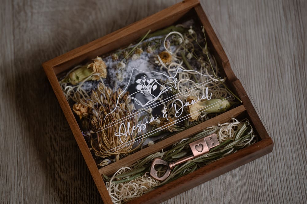 scatola in legno e vetro che contiene la chiavetta USB in cui sono salvate le fotografie del servizio fotografico di matrimonio degli sposi, il coperchio è trasparente e dentro si vedono i fiori del giorno del matrimonio e la foto degli sposi