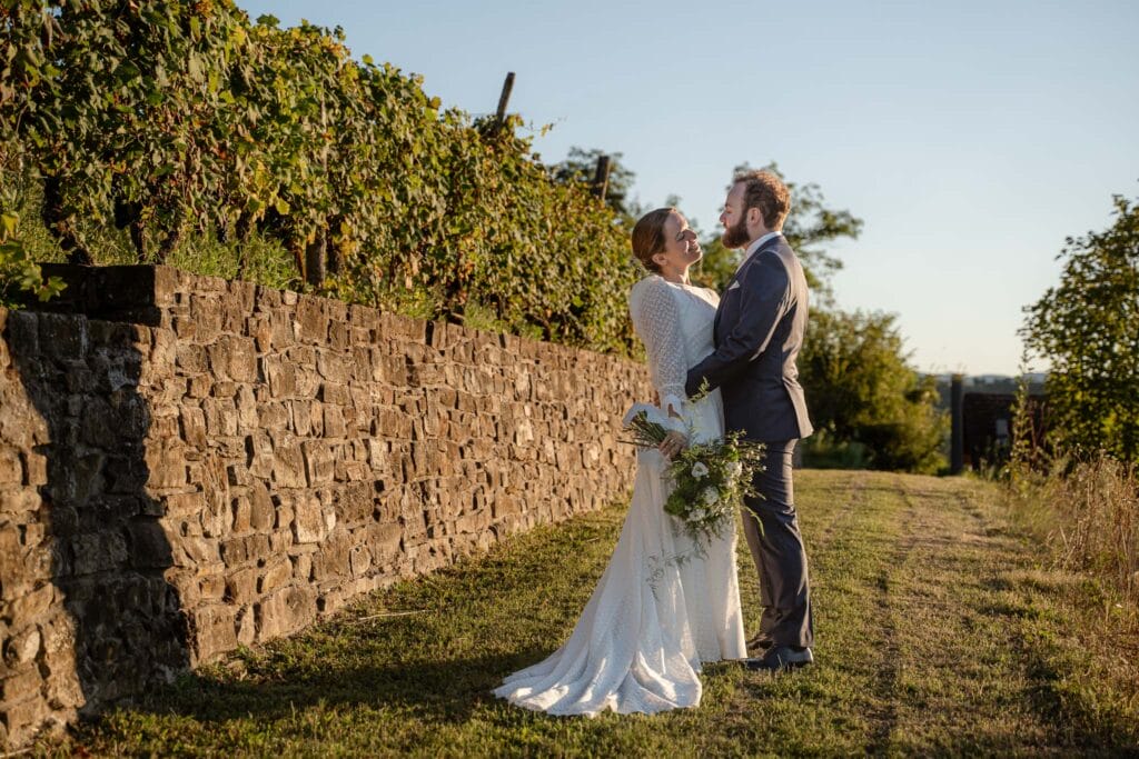 sposi in piedi davanti ad un muro di mattoni, illuminati dalla luce del tramonto, si guardano negli occhi indossano un abito bianco lei e uno blu lui, foto scattata in provincia di Alessandrai dalla fotografa di matrimonio eleonora todaro yelley photography torino