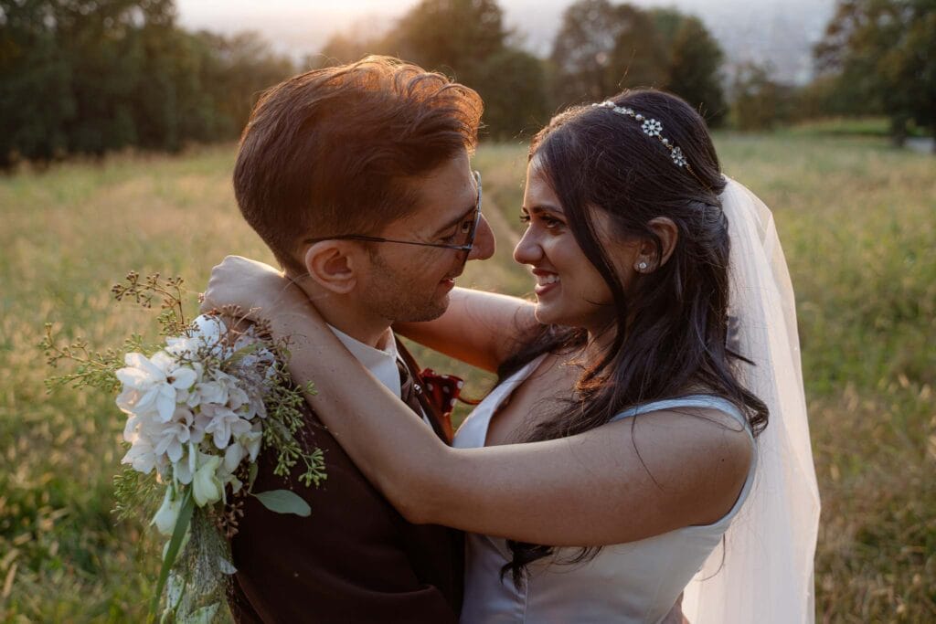coppia di sposi al tramonto al parco san vito di torino durante shooting fotografico di matrimonio scattato dalla fotografa eleonora todaro di yelley photography, lei indossa un abito bianco e lui una giacca marrone, si abbracciano mentre reggono il bouquet in mano