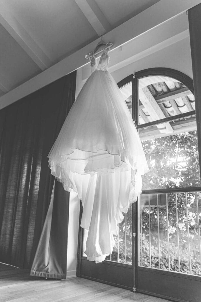 foto in bianco e nero dell'abito della sposa appeso al bastone della tenda alla location la madernassa in piemonte durante servizio fotografico di matrimonio di yelley photography