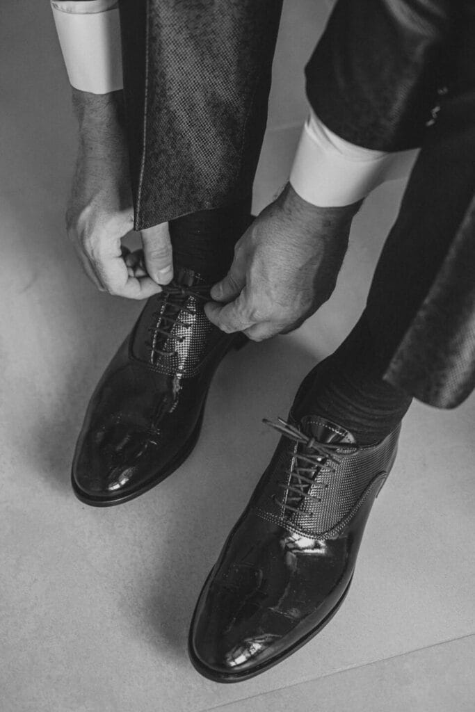 Detail photo of the groom's shoes tied by his hands, black and white, during wedding photo shoot for bride and groom preparations