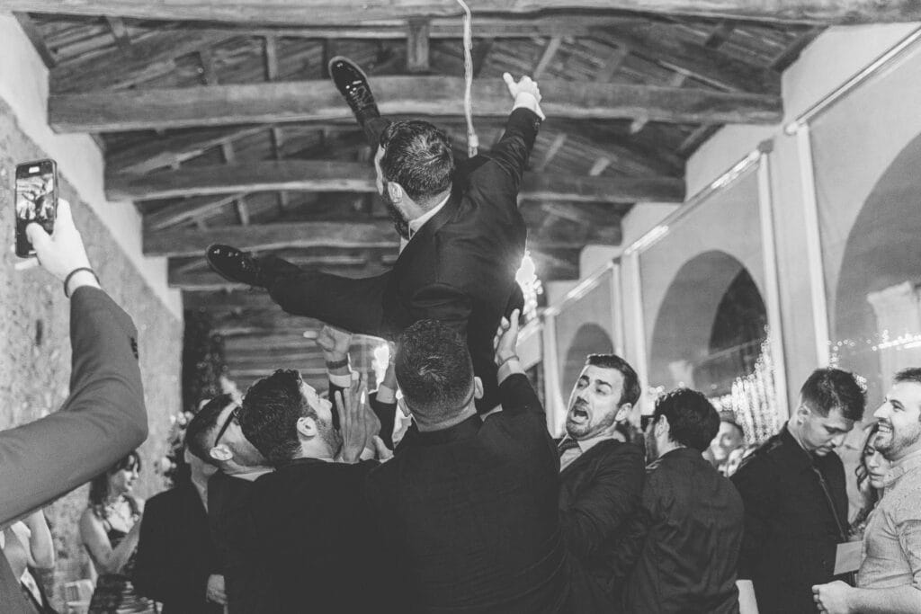 foto in bianco e nero di dettaglio di uno sposo lanciato in aria dai suoi amici mentre festeggia il matrimonio durante il servizio fotografico di yelley photography