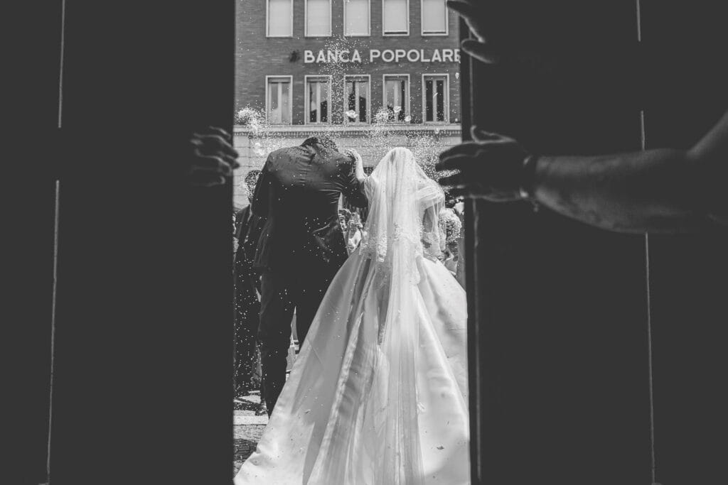 foto di dettaglio di due sposi che escono dalla chiesa e vengono accolti dal lancio del riso durante servizio fotografico di matrimonio di yelley photography, si vedono anche due mani che stanno per chiudere il portone di legno della chiesa