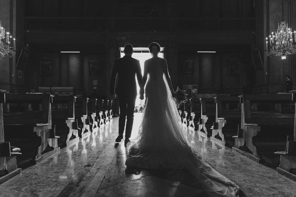 Foto in bianco e nero di una coppia di sposi visti da dietro dentro una chiesa che si avviano all'uscita per il lancio del riso, scattata durante servizio fotografico di matirmonio di yelley photography