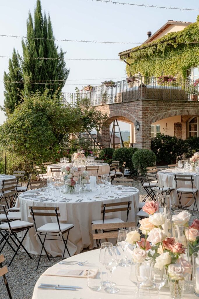 dettaglio della location di matrimonio con i tavoli imbanditi e i fiori come decorazione durante servizio fotografico di matrimonio, nello sfondo si vedono degli alberi alti, il cielo azzurro e una struttura in mattoni rustica