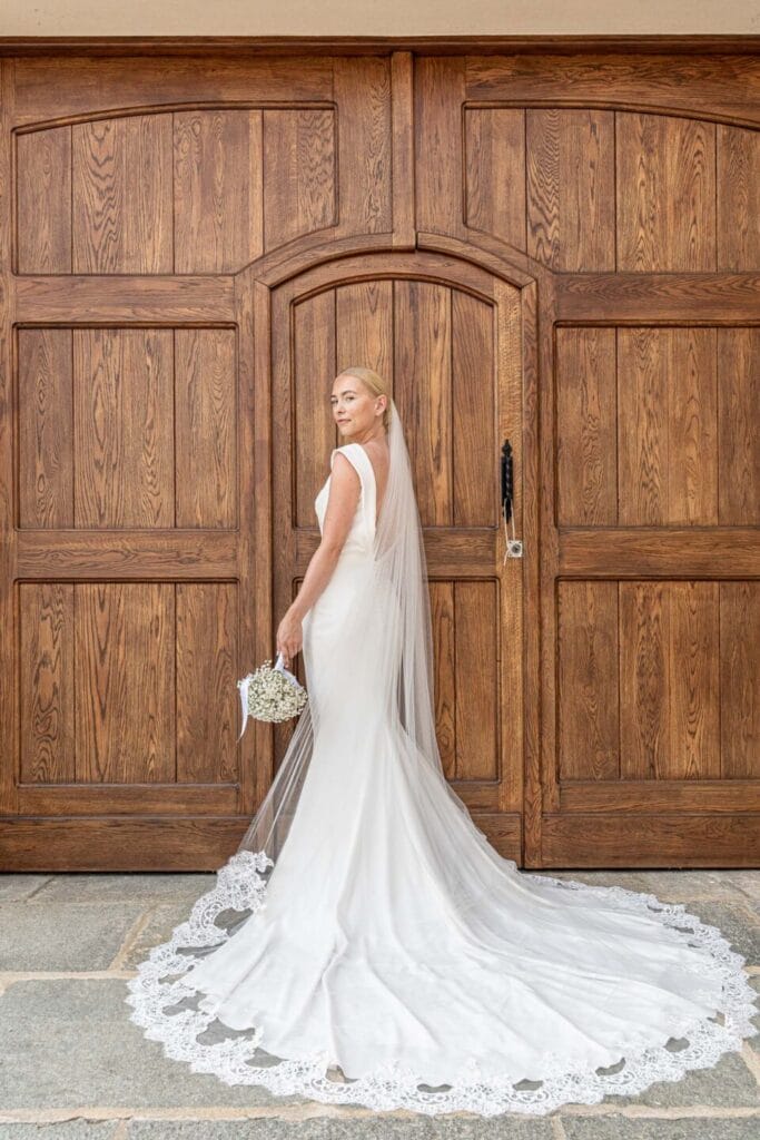 foto della sposa di spalle davanti ad un portone di legno con l'abito a sirena aperto e il velo ben sistemato sulla coda dell'abito durante servizio fotografico di matrimonio