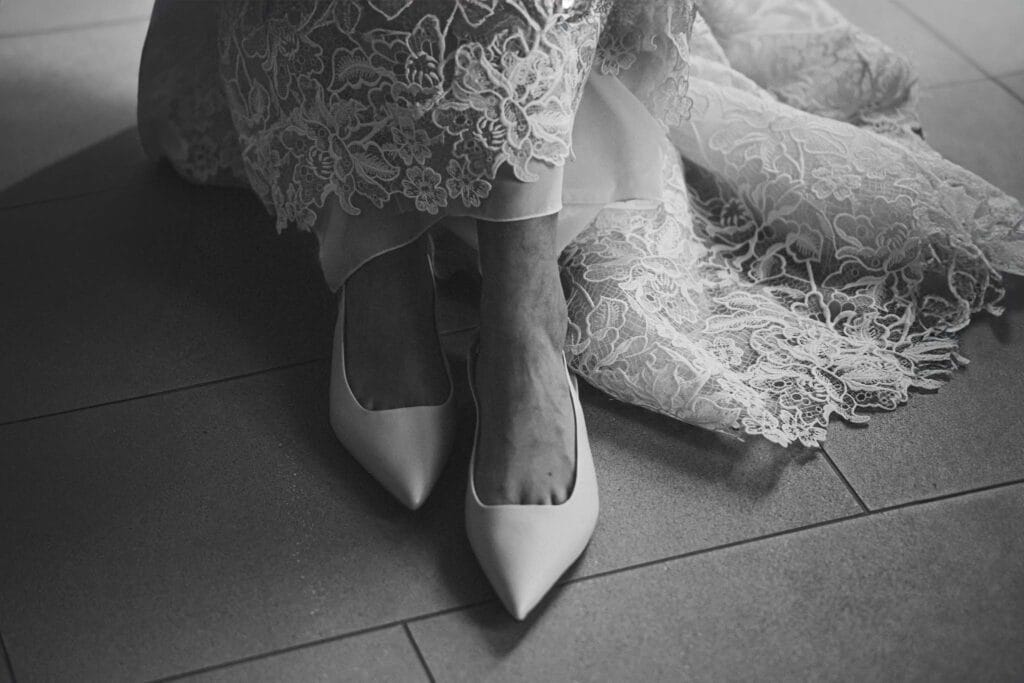 foto in bianco e nero di dettaglio delle scarpe di una sposa durante servizio fotografico di matrimonio, le scarpe sono a punta e si vede un pezzo di strascico