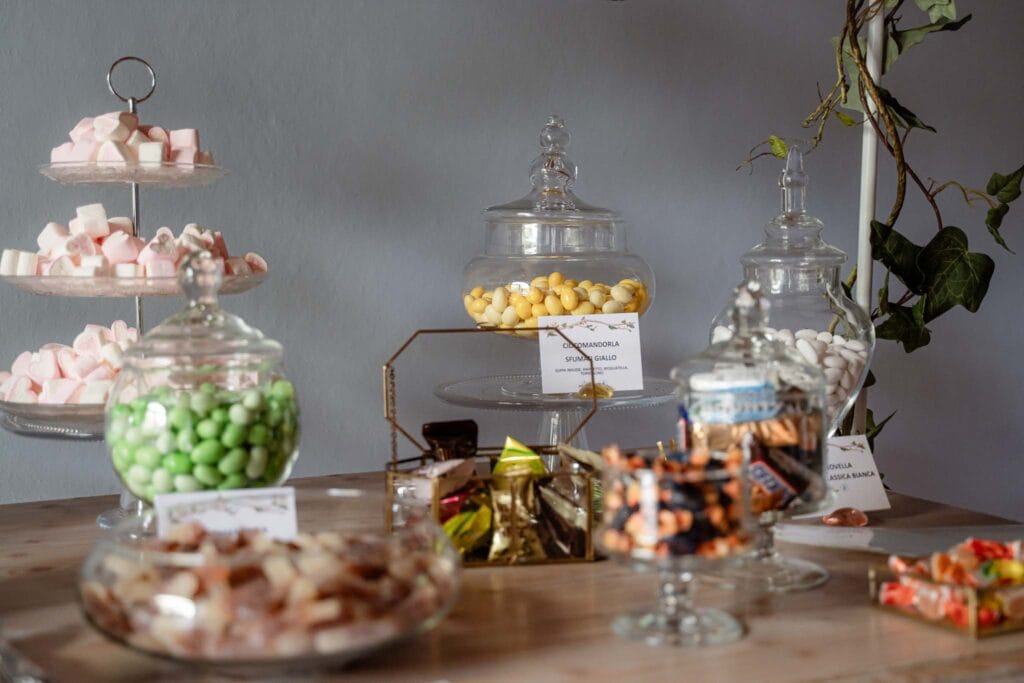 foto della confettata di matirmonio parte delle bomboniere originali, sul tavolo si vedono tanti vasi trasparenti con confetti e caramelle colorate fotografata durante il servizio di matrimonio
