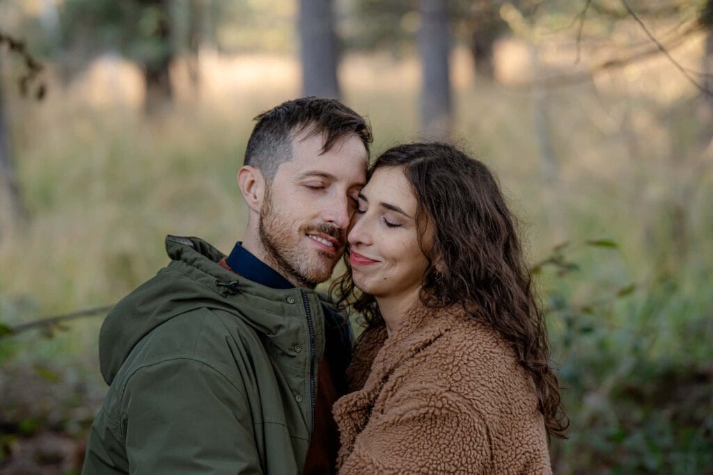 Coppia durante servizio prematrimoniale in mezzo al bosco in autunno, sono con i visi vicini e indossano un cappotto verde lui e marrone lei