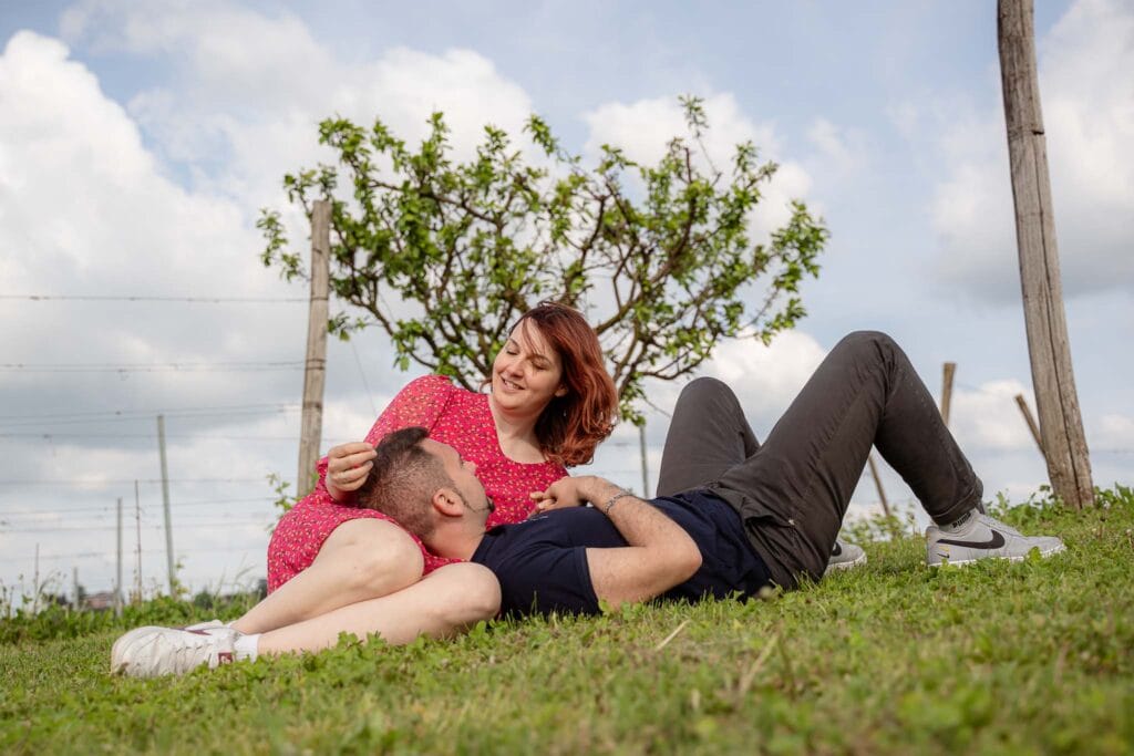 Coppia durante prematrimoniale in primavera sono su un prato con il cielo azzurro alle spalle, lei ha un abito rosa e lui jean e maglietta neri, si stanno coccolando nel prato durante shooting di yelley photography