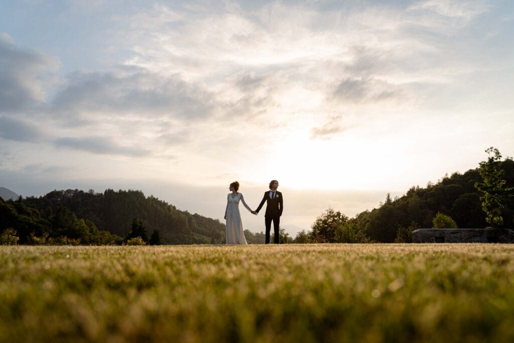 coppia davanti al tramonto presso chiusa di pesio, villa san lorenzo, mentre si tiene per mano vestiti da sposi durante servizio fotografico di matirmonio di yelley photography